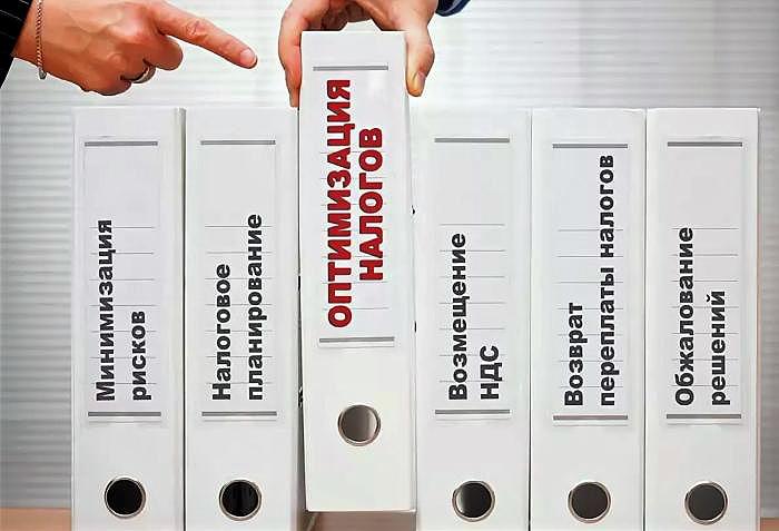 Папки-регистраторы с ярлыками услуг налоговой оптимизации: «Минимизация рисков», «Налоговое планирование», «Оптимизация налогов», «Возмещение НДС», «Возврат переплаты налогов», «Обжалование решений» — рука указывает на папку «Оптимизация налогов»